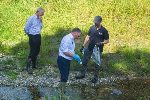 Three people stand beside the Chamber Mead wetland testing the water quality.