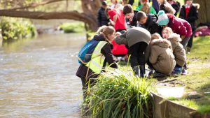 A group of school children standing along the river bank.