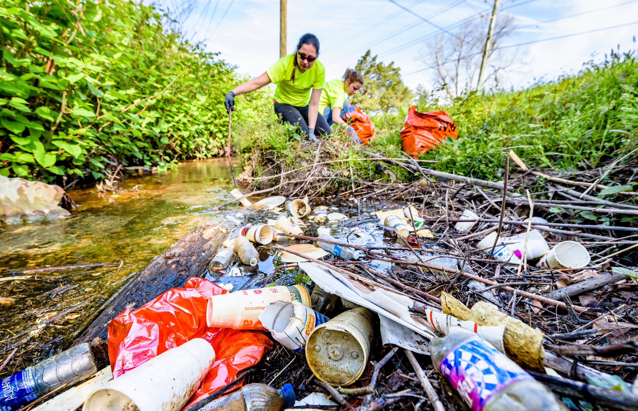 Two volunteers are removing litter from a stream, helping to keep the water clean and promote a healthier ecosystem.